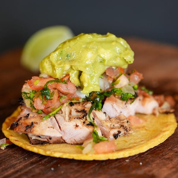 A grilled chicken taco from La Chancla Mexican Grill, topped with guacamole, pico de gallo, and a lime wedge.