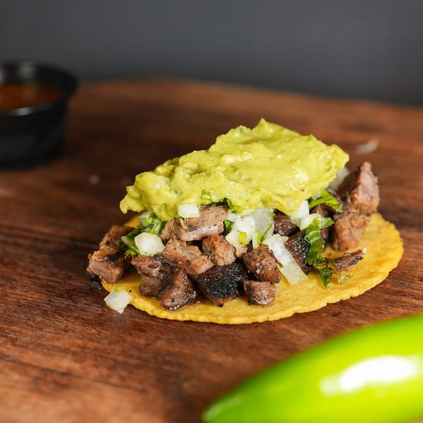 A La Chancla Mexican Grill carne asada taco with guacamole, onions, and cilantro on a wooden surface.