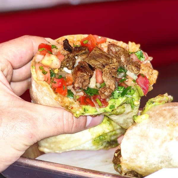 Hand holding a La Chancla Mexican Grill burrito, overflowing with steak, pico de gallo, and guacamole.