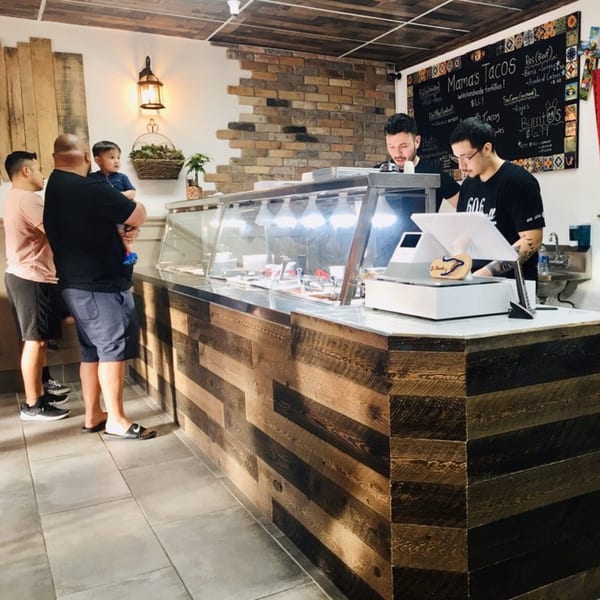 Customers ordering at the counter of La Chancla Mexican Grill, with a menu board in the background.