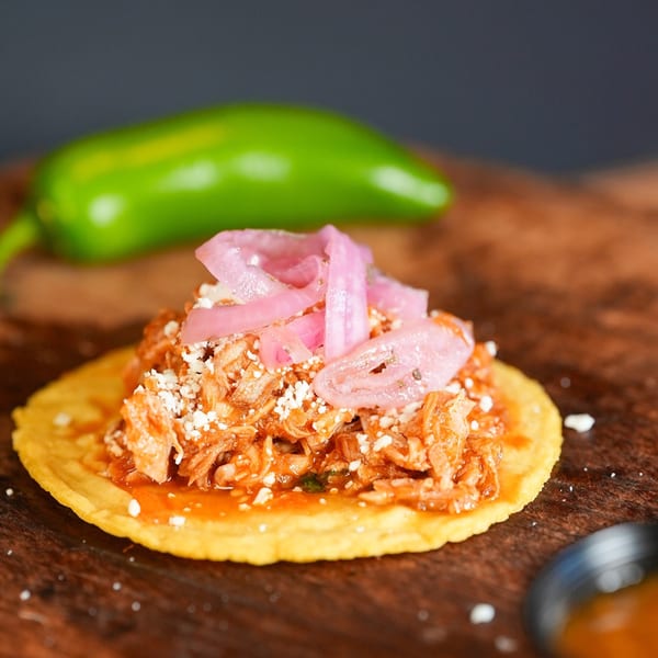 A La Chancla Mexican Grill tostada with shredded meat, red sauce, cheese, and pickled onions.