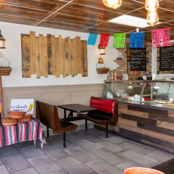Interior of La Chancla Mexican Grill with colorful papel picado, wooden decor, and a food counter.