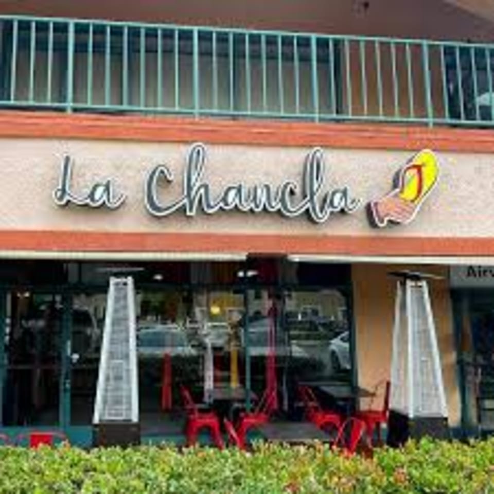 Exterior of La Chancla Mexican Grill with outdoor seating, red chairs, and patio heaters.