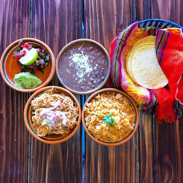 La Chancla Mexican Grill's Mexican feast with salsa, guacamole, beans, shredded chicken, rice, and tortillas.