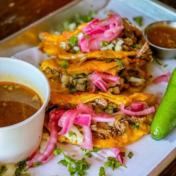 Three birria tacos with pickled red onions, cilantro, and a side of consommé.